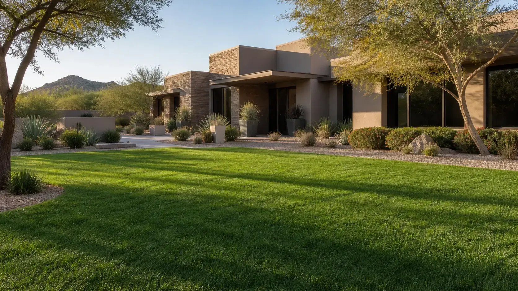 Single-story modern house with stone accents and a green lawn in a desert landscape