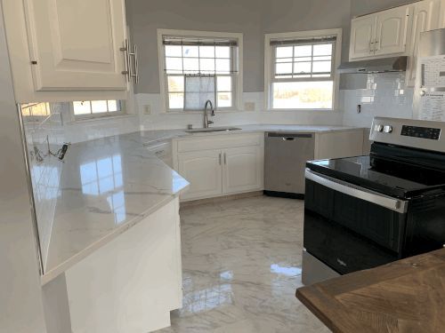 A kitchen with white cabinets , a stove , a sink , and a window.