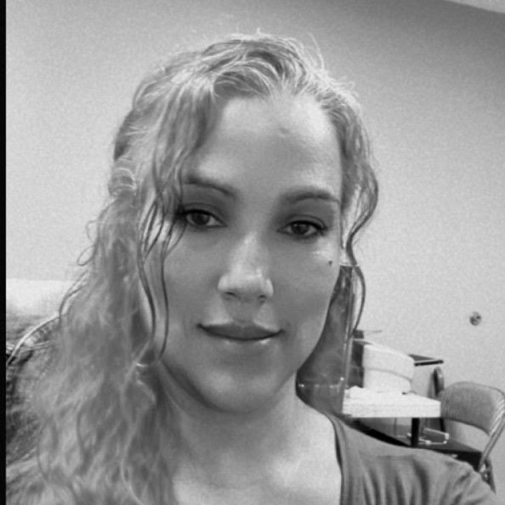 Black-and-white close-up selfie of a person with wavy hair and a slight smile indoors