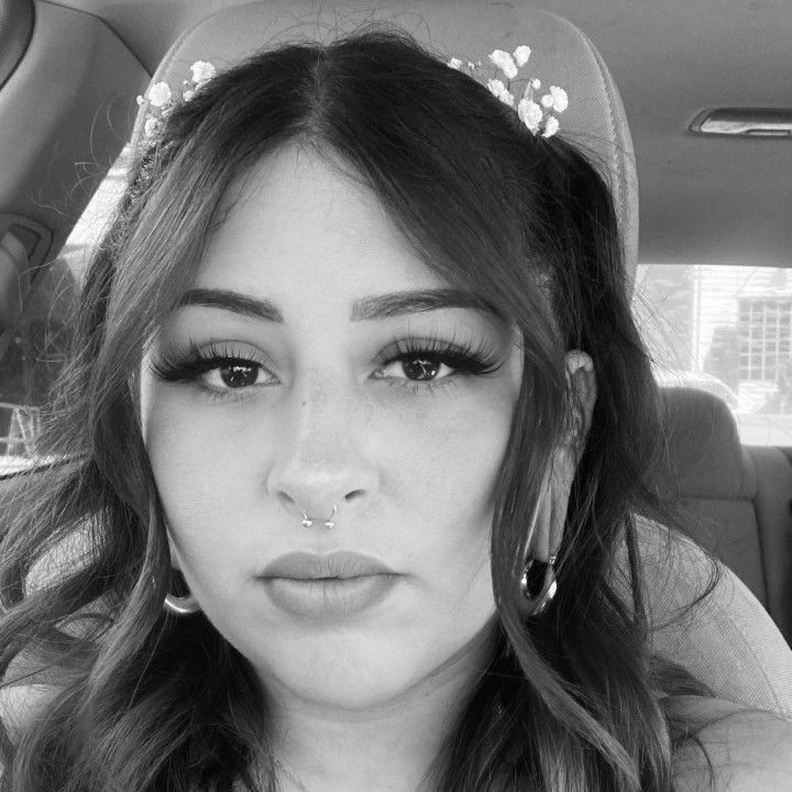 Black-and-white selfie of a person with wavy hair and hoop earrings, sitting in a car.