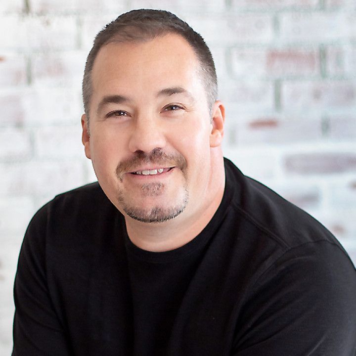 Smiling man in a black shirt against a light brick wall background