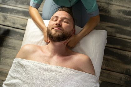 Man lying on a massage table with eyes closed while receiving a neck massage