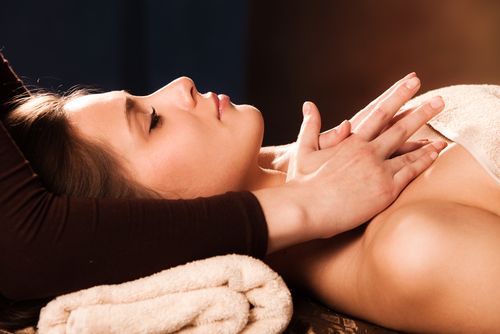 Woman lying face down during a spa massage, with folded towels and hands resting on her back