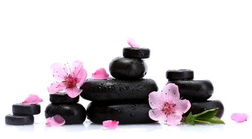 Stacked black spa stones with pink cherry blossoms and petals on a white background