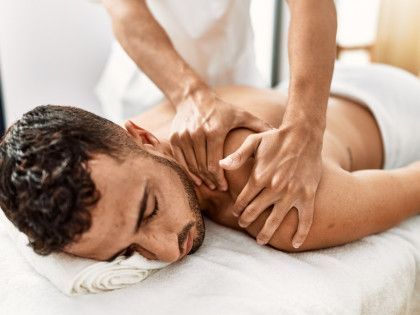 Massage therapist kneading a man’s shoulders as he lies face down on a spa table