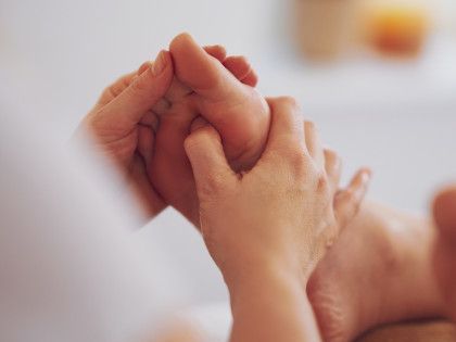 Hands gently holding and massaging a baby’s foot in a soft, warm setting