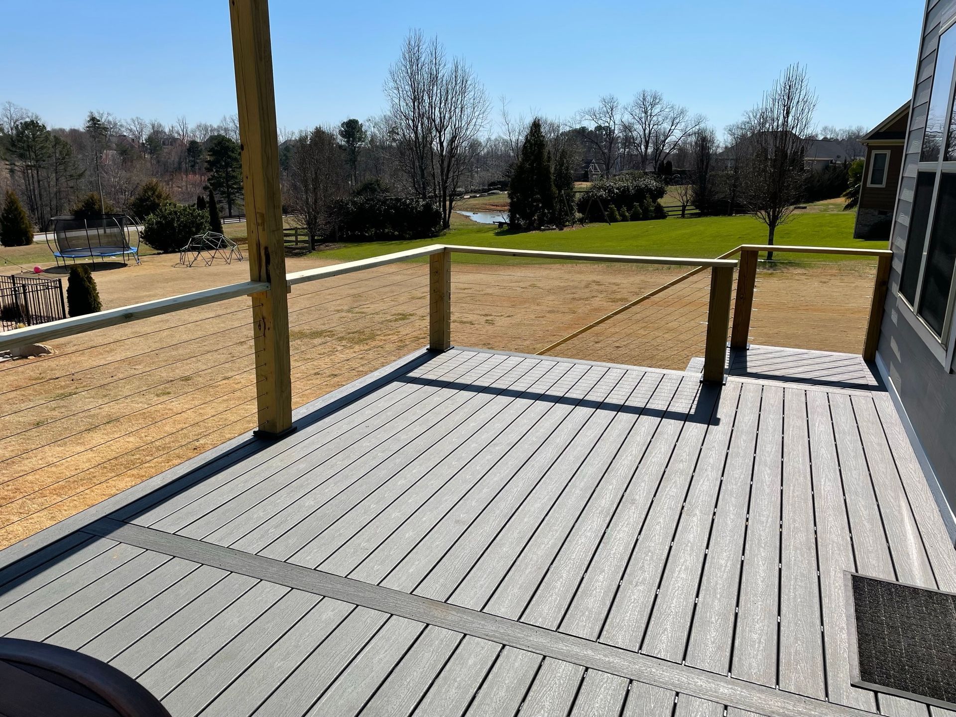 A gray deck with a wooden railing and a view of a field.