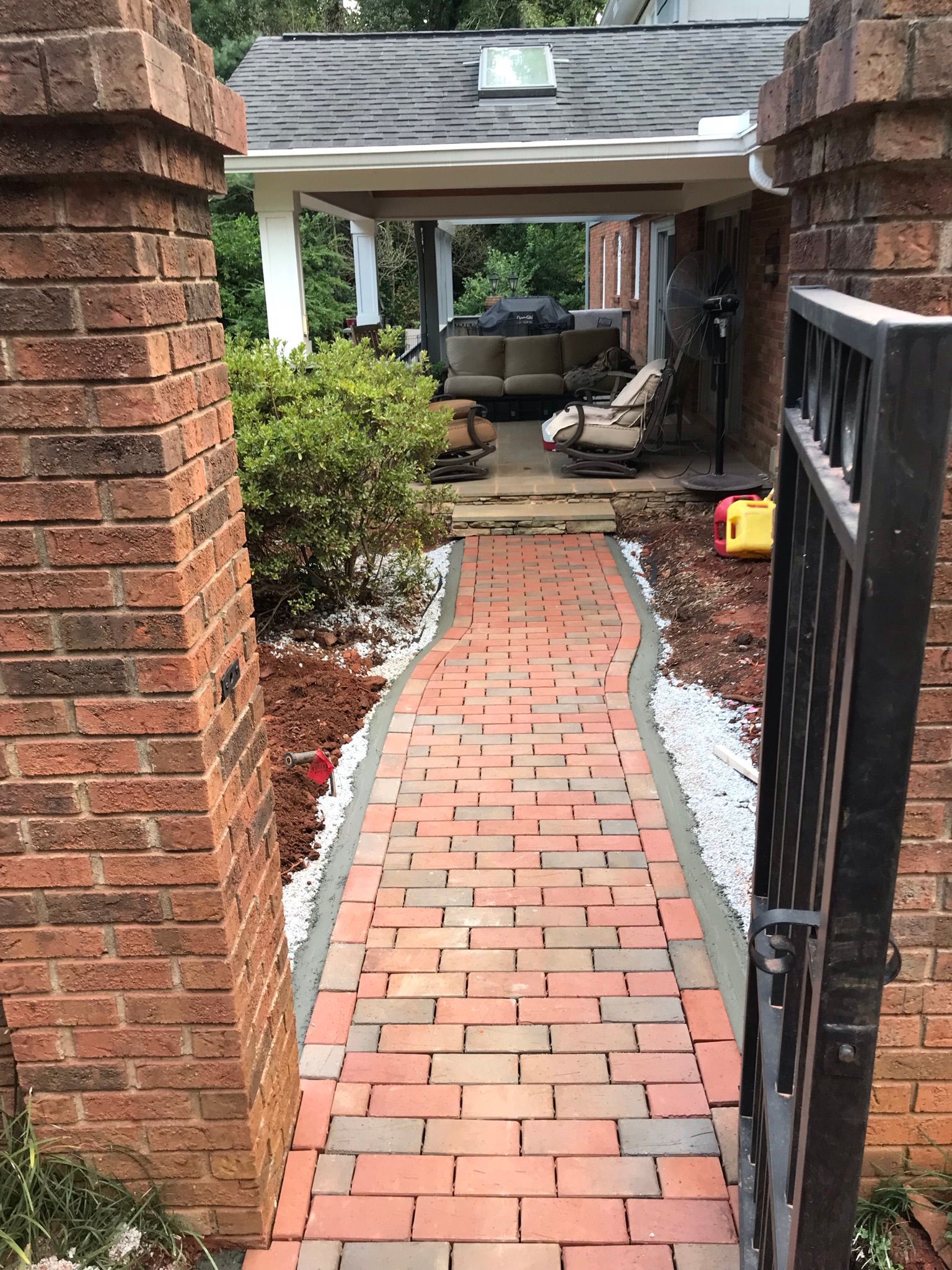 A brick walkway leading to a house with a gate open.