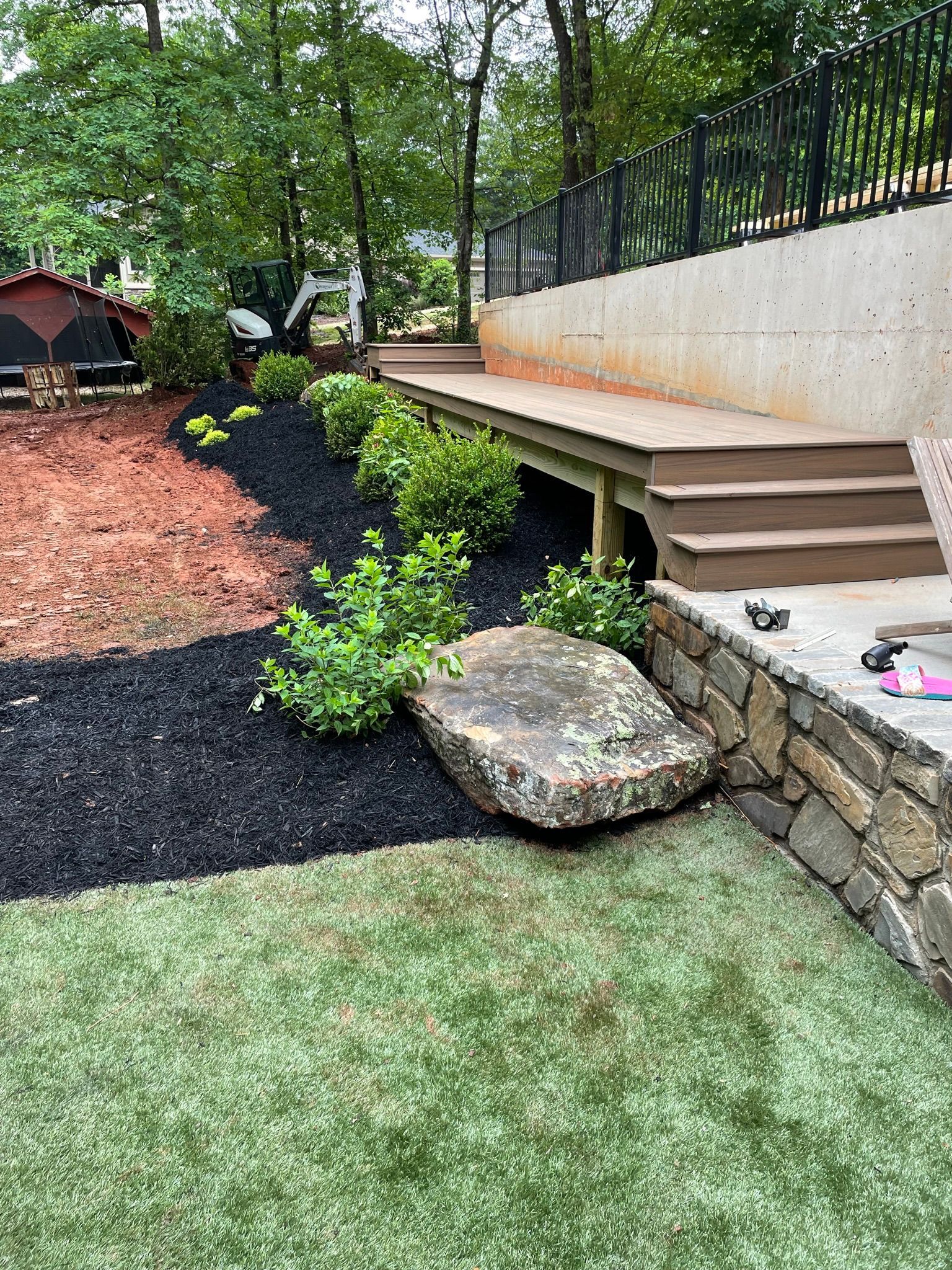 A large rock is sitting on top of a lush green lawn next to a stone wall.