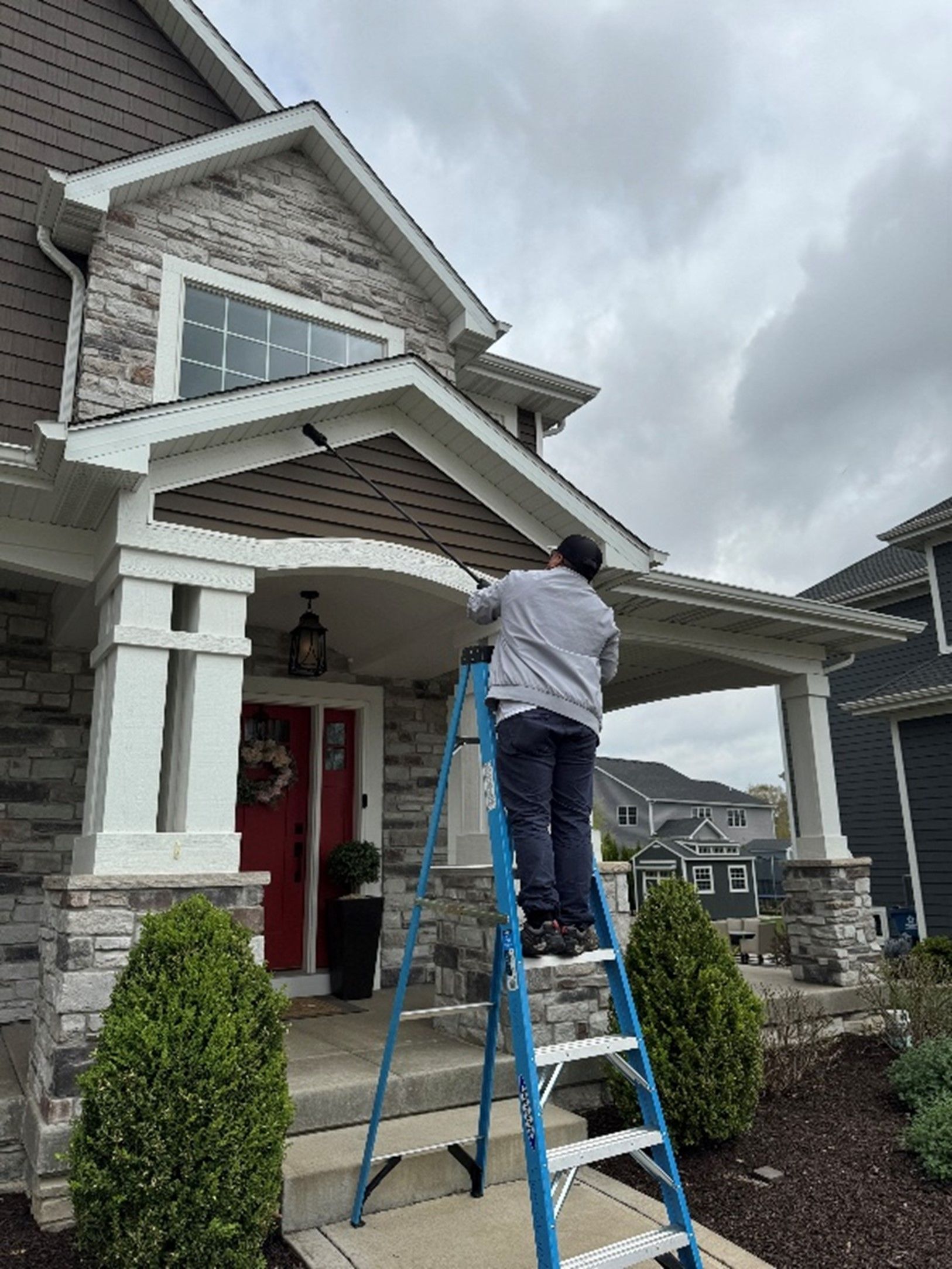 A man is standing on a ladder in front of a house. | Residential Pest Control Services Flossmoor, IL