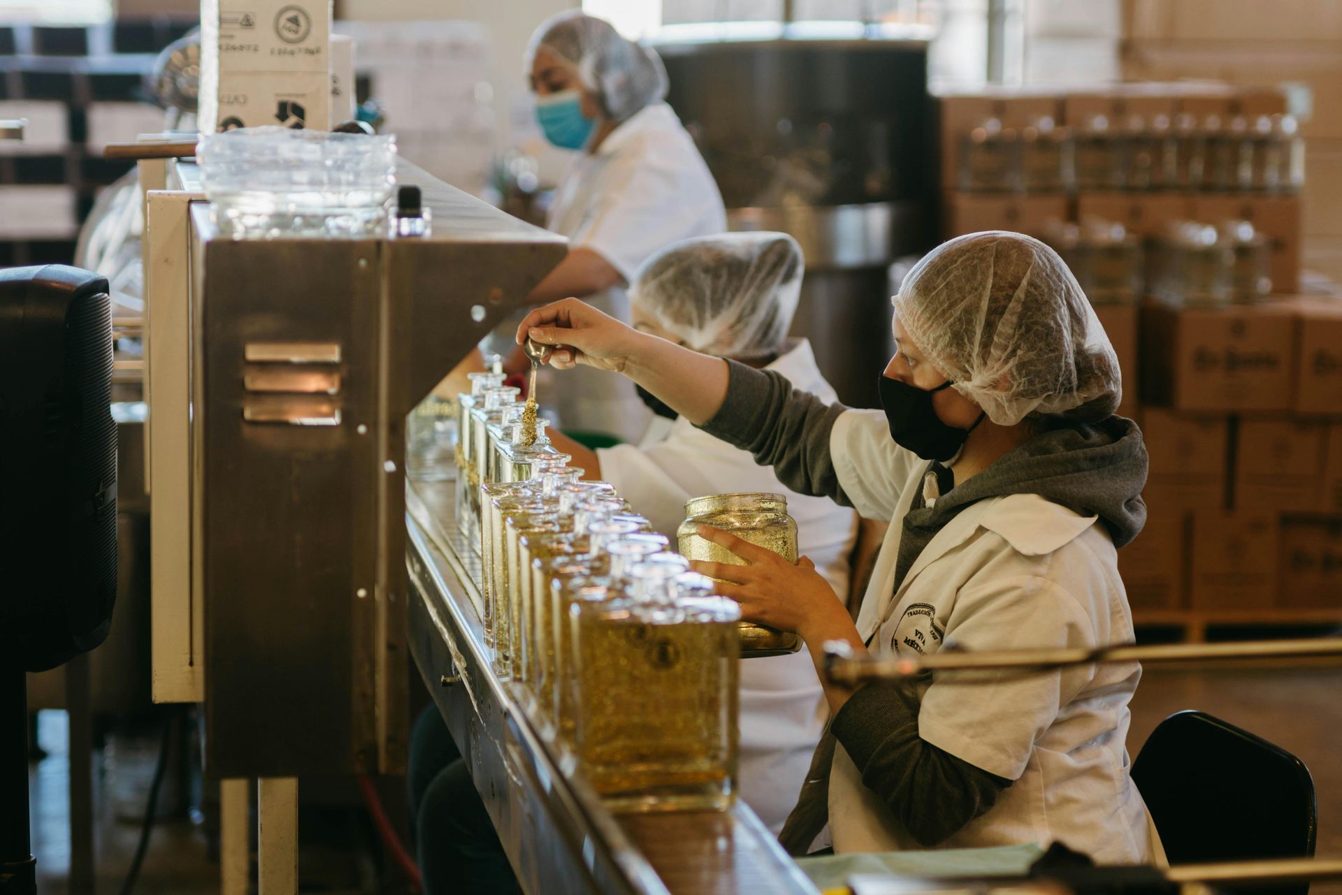 En una fábrica, unos trabajadores embotellan aceite en una cadena de montaje, con filas de botellas llenas en primer plano.