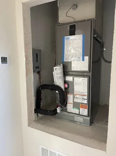 Furnace in an unfinished wall cutout. Includes black tubing, electrical box, and paperwork.