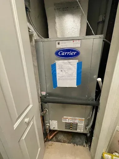 A Carrier HVAC unit in a utility closet with a white door to the left.