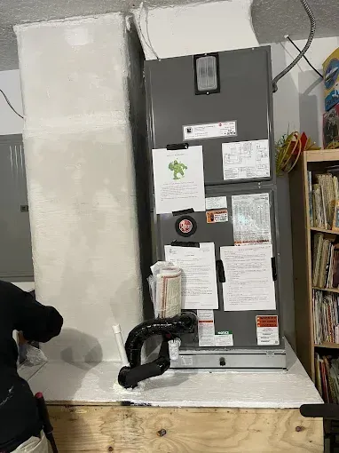 HVAC unit with ductwork and a person working on the unit in an indoor setting.
