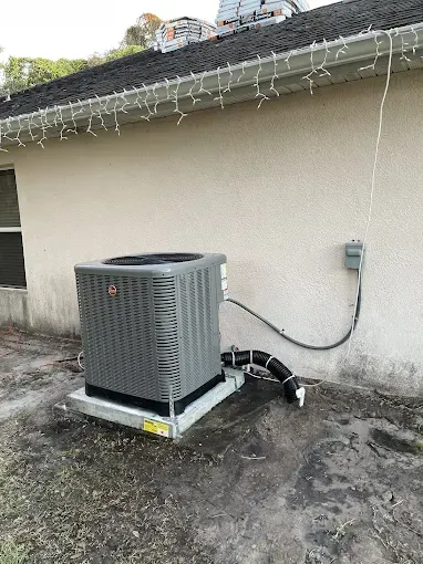An air conditioning unit on a concrete pad next to a light-colored building.