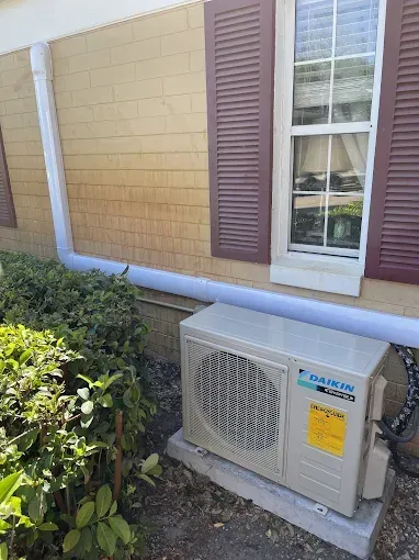 Daikin air conditioning unit outside a building with brown shutters and yellow siding.
