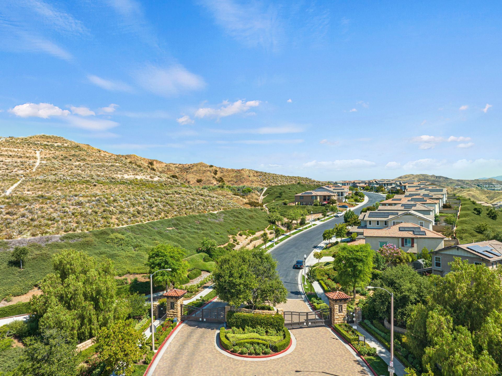 Aerial view of a winding suburban road and residential community nestled against a sunny hillside.