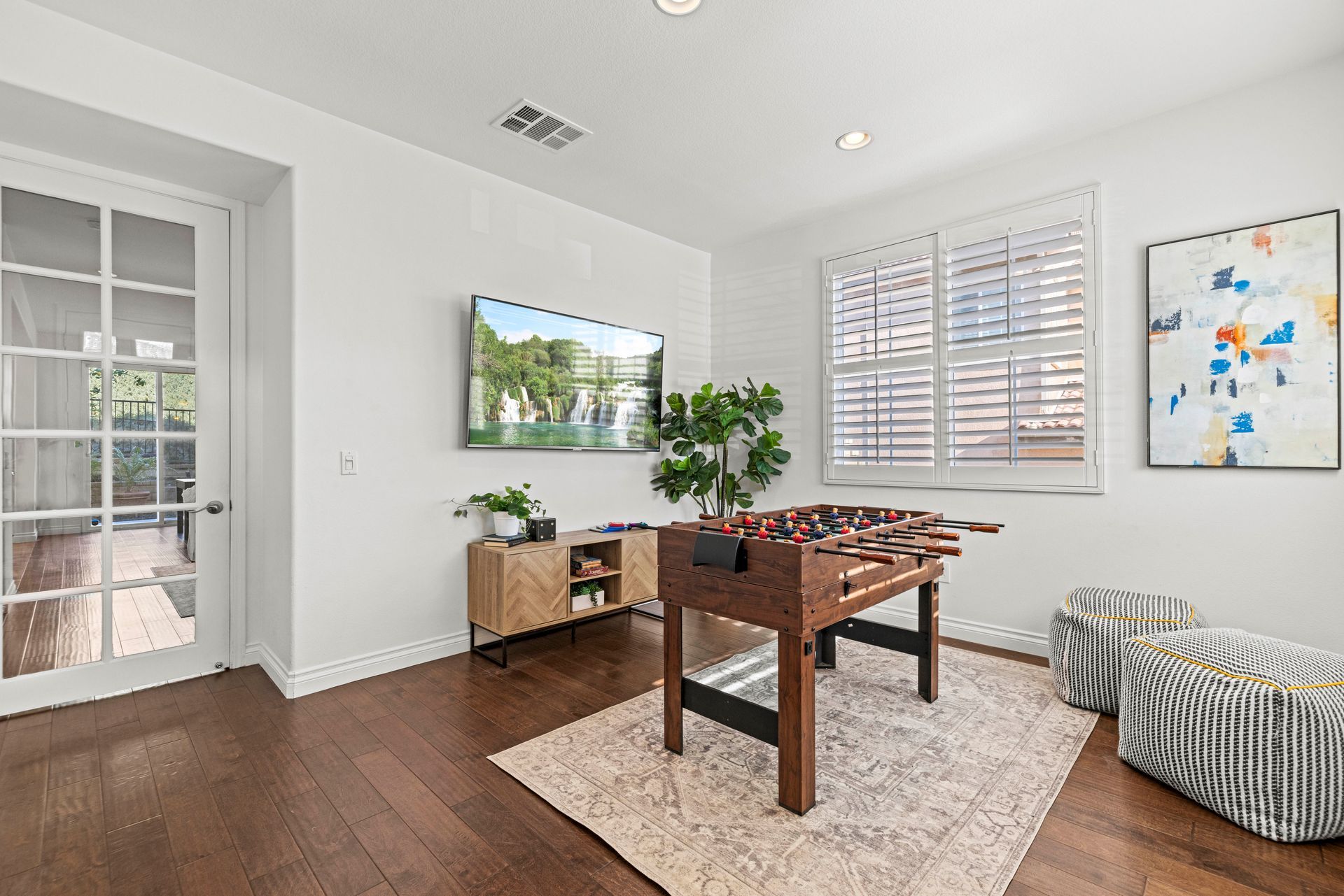 Sunlit interior flex space featuring a dark wood foosball table, patterned stools, and a gold console table.