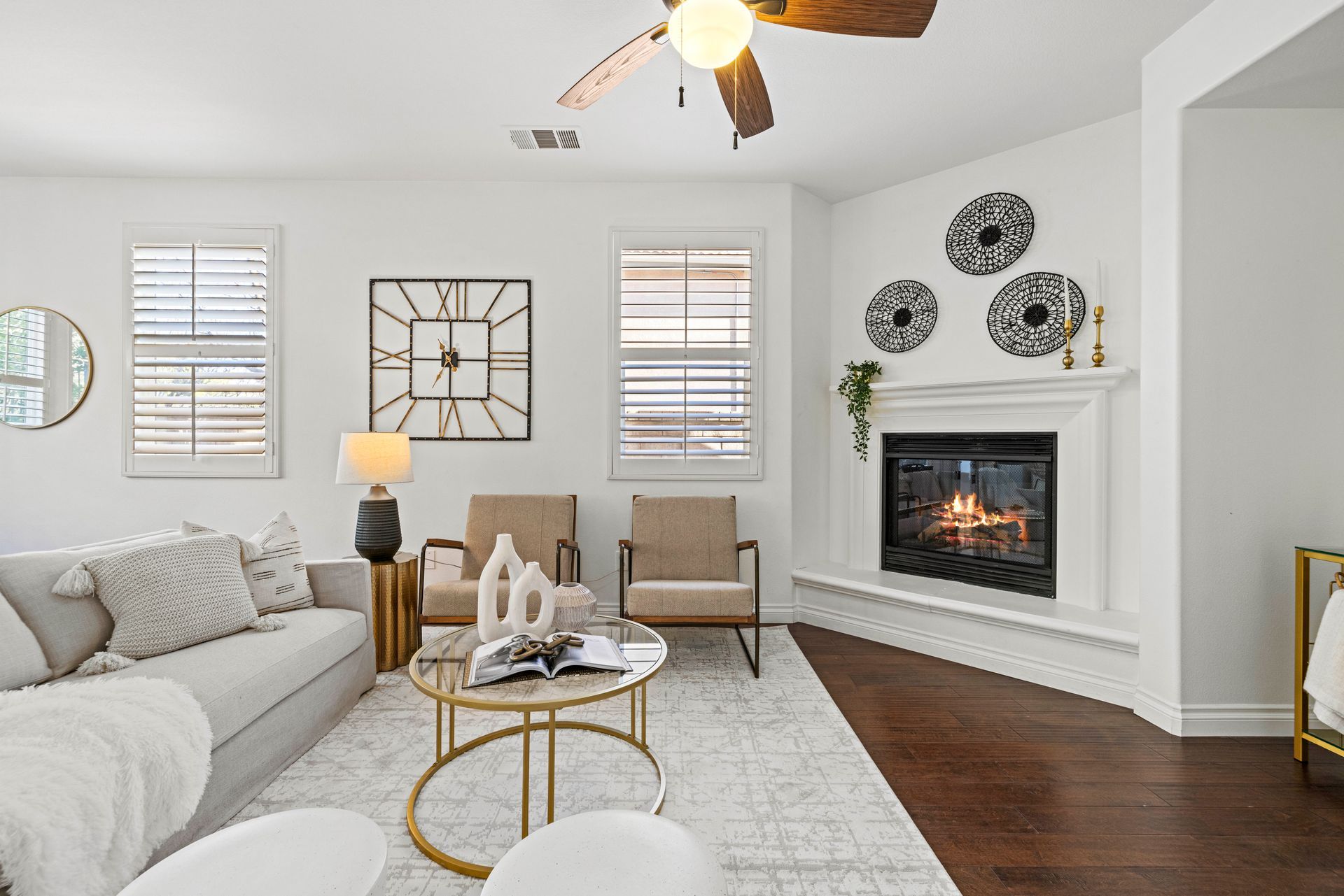 Cozy living room featuring a lit fireplace, comfortable armchairs, a glass coffee table, and a ceiling fan.