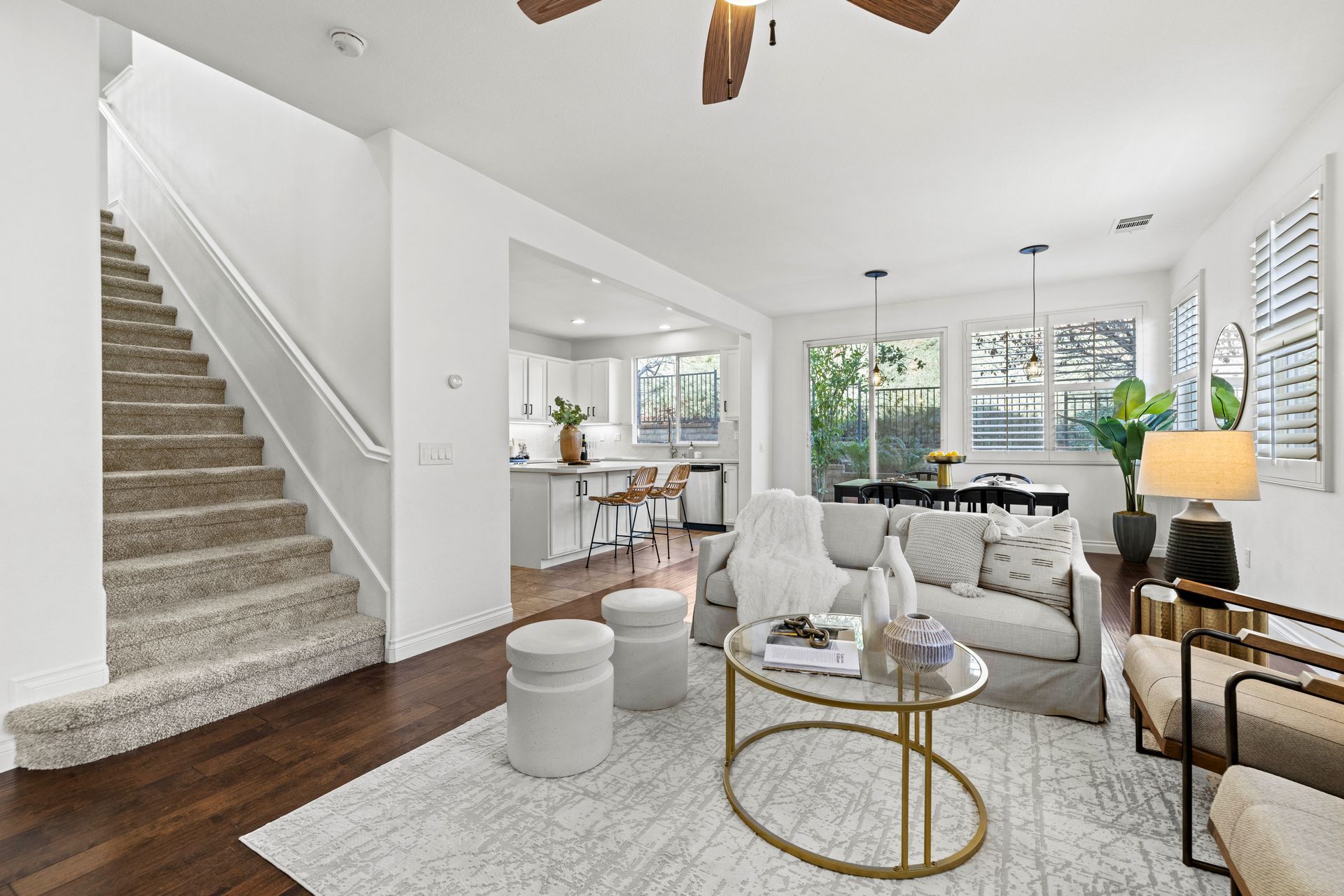 Light-filled living room view showing a carpeted staircase, hardwood flooring, and adjacent open kitchen.