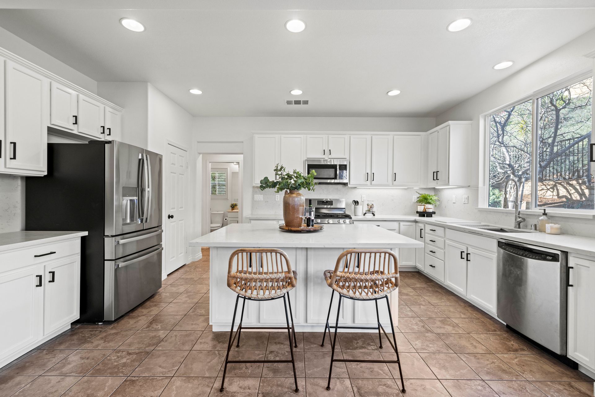 Modern kitchen featuring white cabinetry, stainless steel appliances, and a center island with woven barstools.