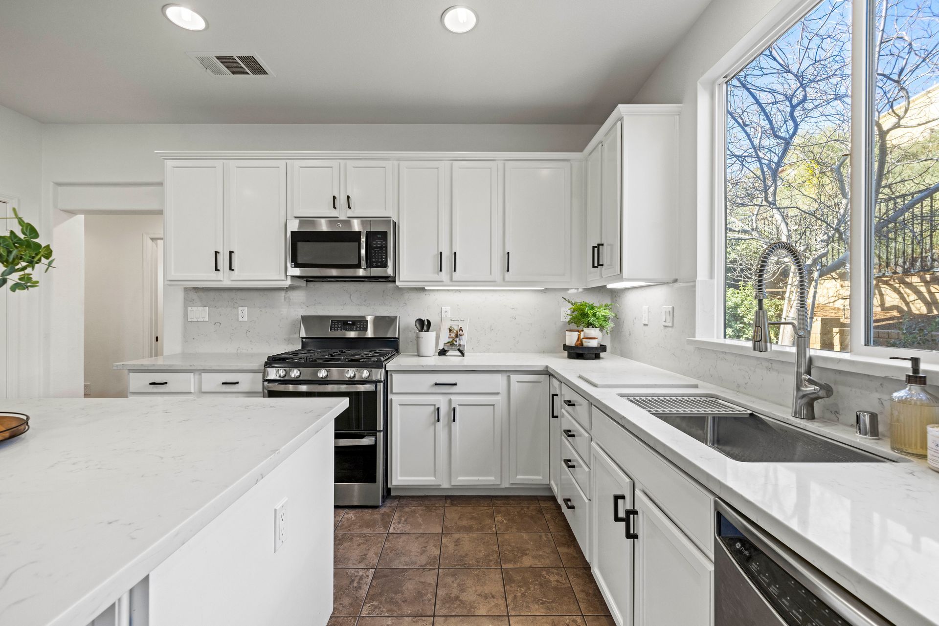 An all-white modern kitchen that has a window providing natural light with a dishwasher, oven, and microwave | Sell my home fast in Santa Clarita, CA