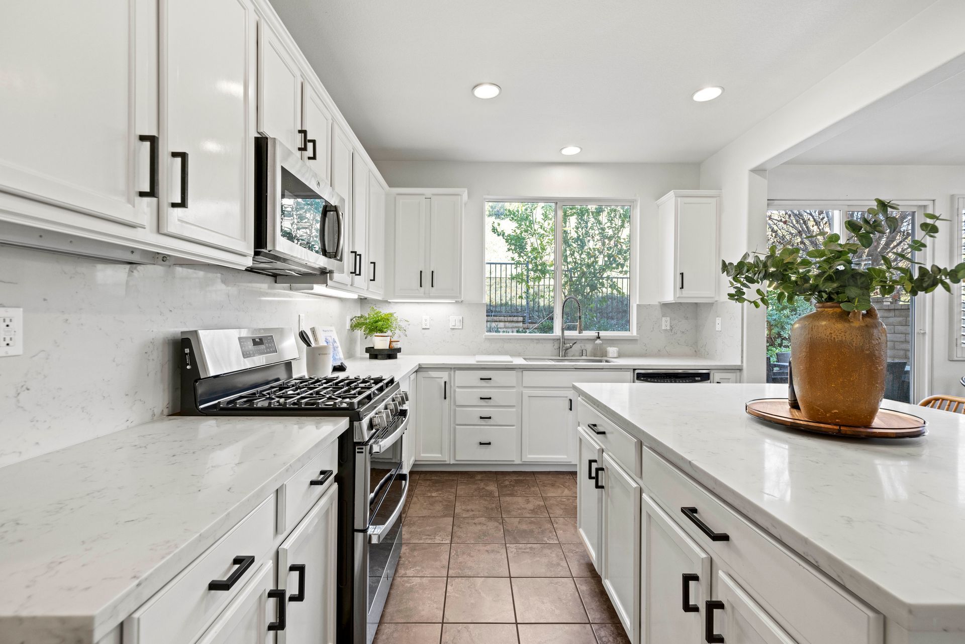 Brightly lit, all-white, and spacious modern kitchen with large windows, kitchen appliances, and kitchen island. | Homes for sale in Santa Clarita.