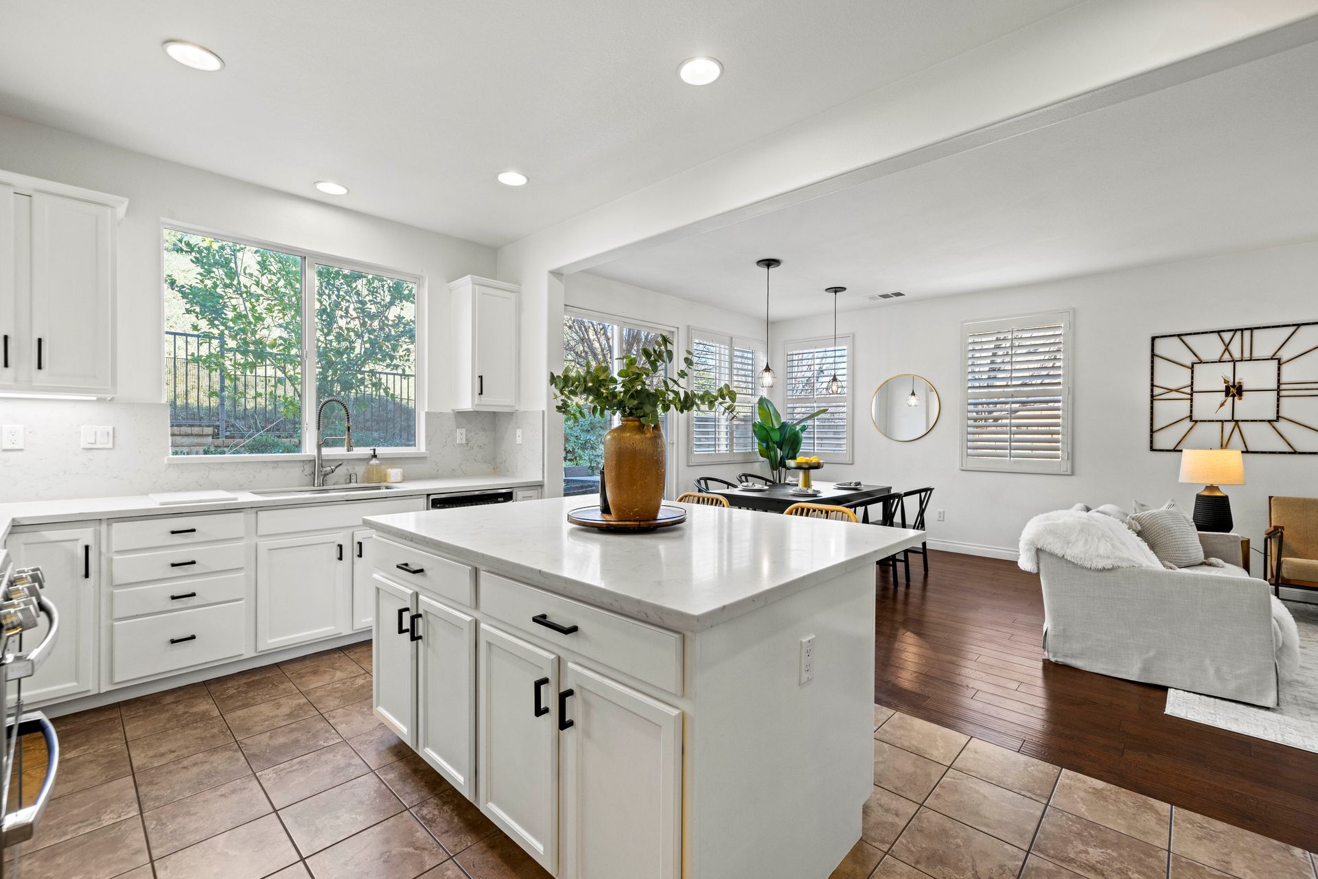 A kitchen island with a large potted plant that connects to a living room that’s decorated with paintings.