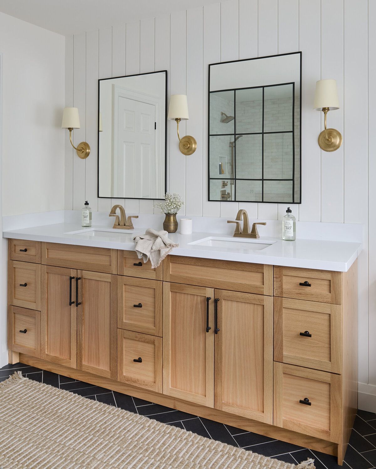 Bathroom vanity with light wood cabinets, two mirrors, sconces, and white countertop.