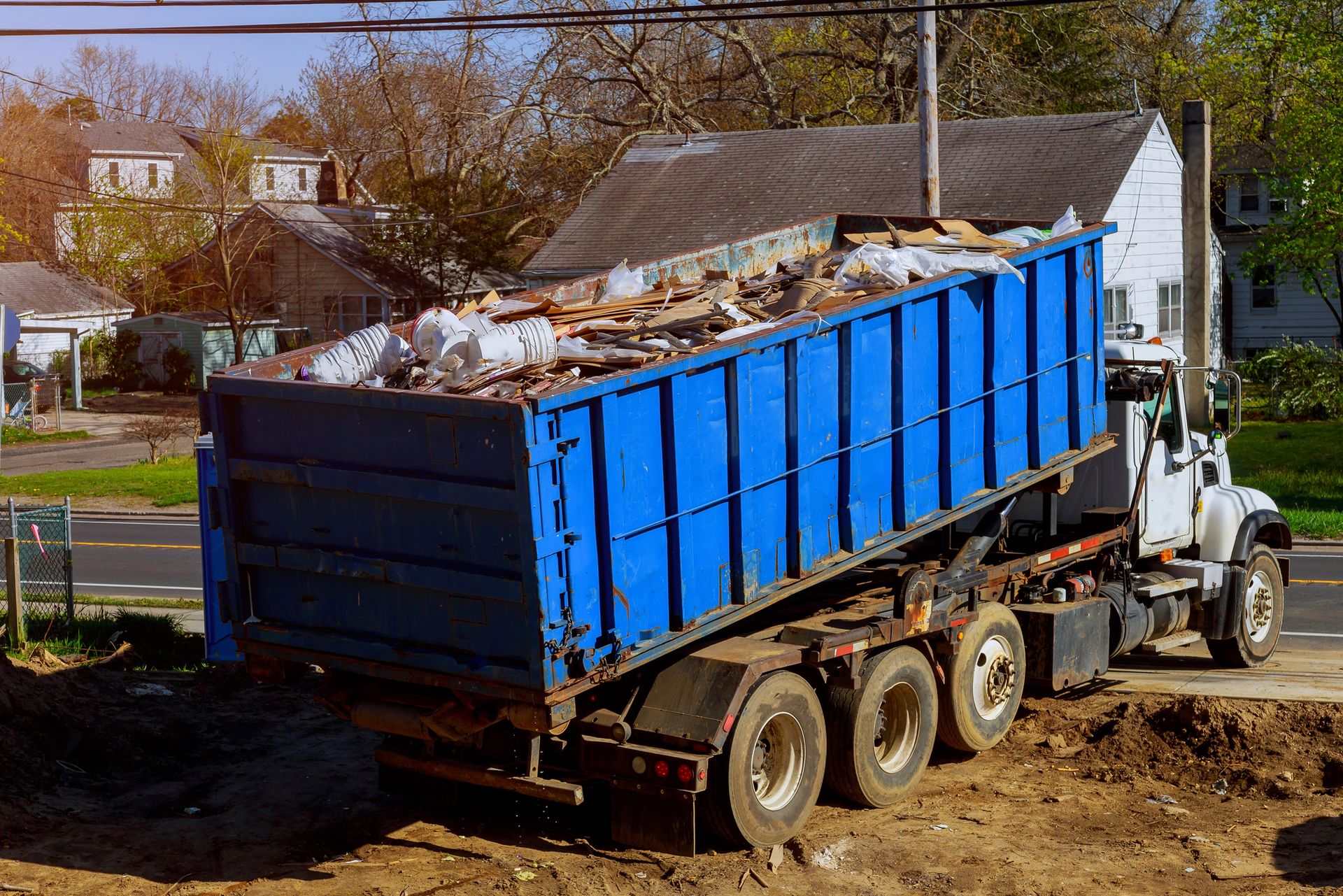 Blue dumpster loaded with debris being hauled by a white truck at a construction site.