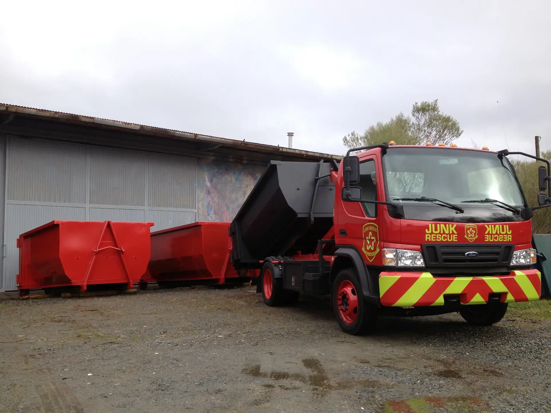 Red dumpster truck with two red dumpsters; parked in front of a building.