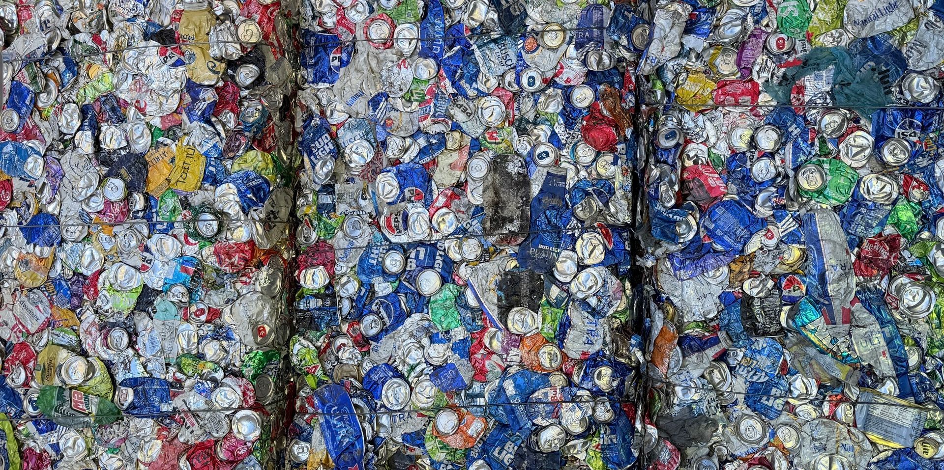 A compressed bale of crushed aluminum cans; many colors are visible, including blue, white, and red.