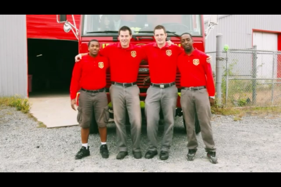 Four people in red shirts and khaki pants pose in front of a fire truck.
