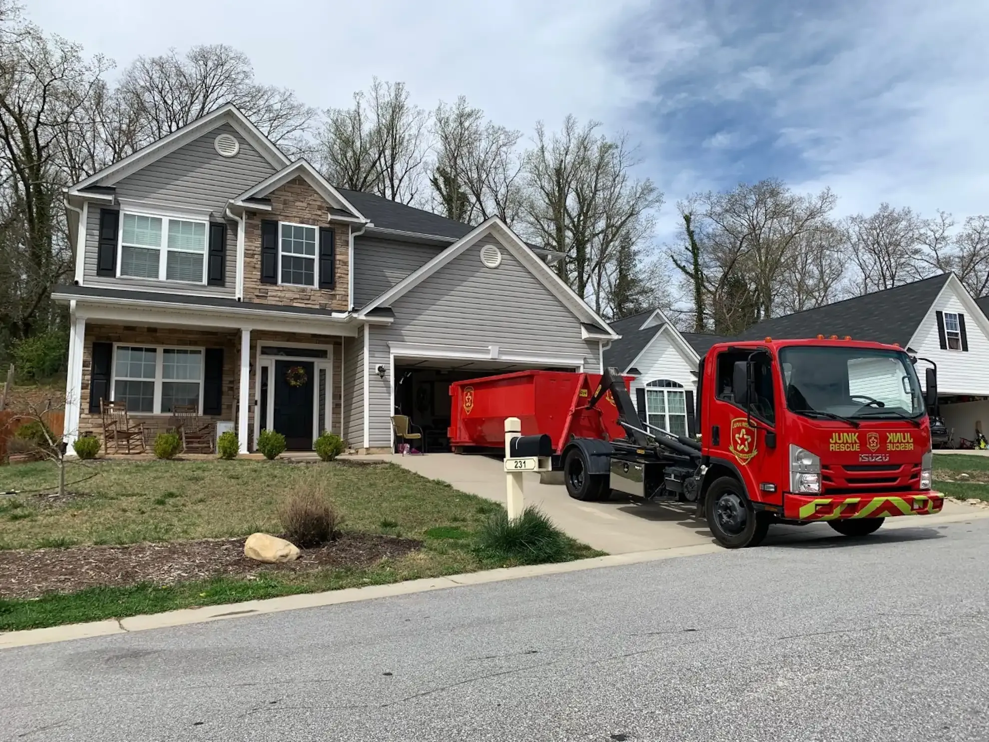 Red dump truck with raised container next to two red dumpsters; parked in front of a gray building.