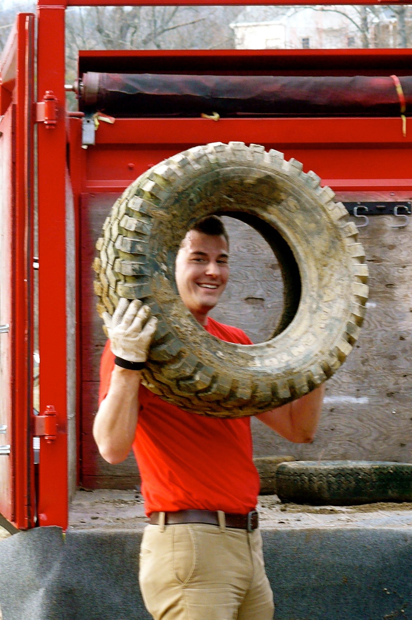 Man holding large tire, smiling, in front of a red machine.