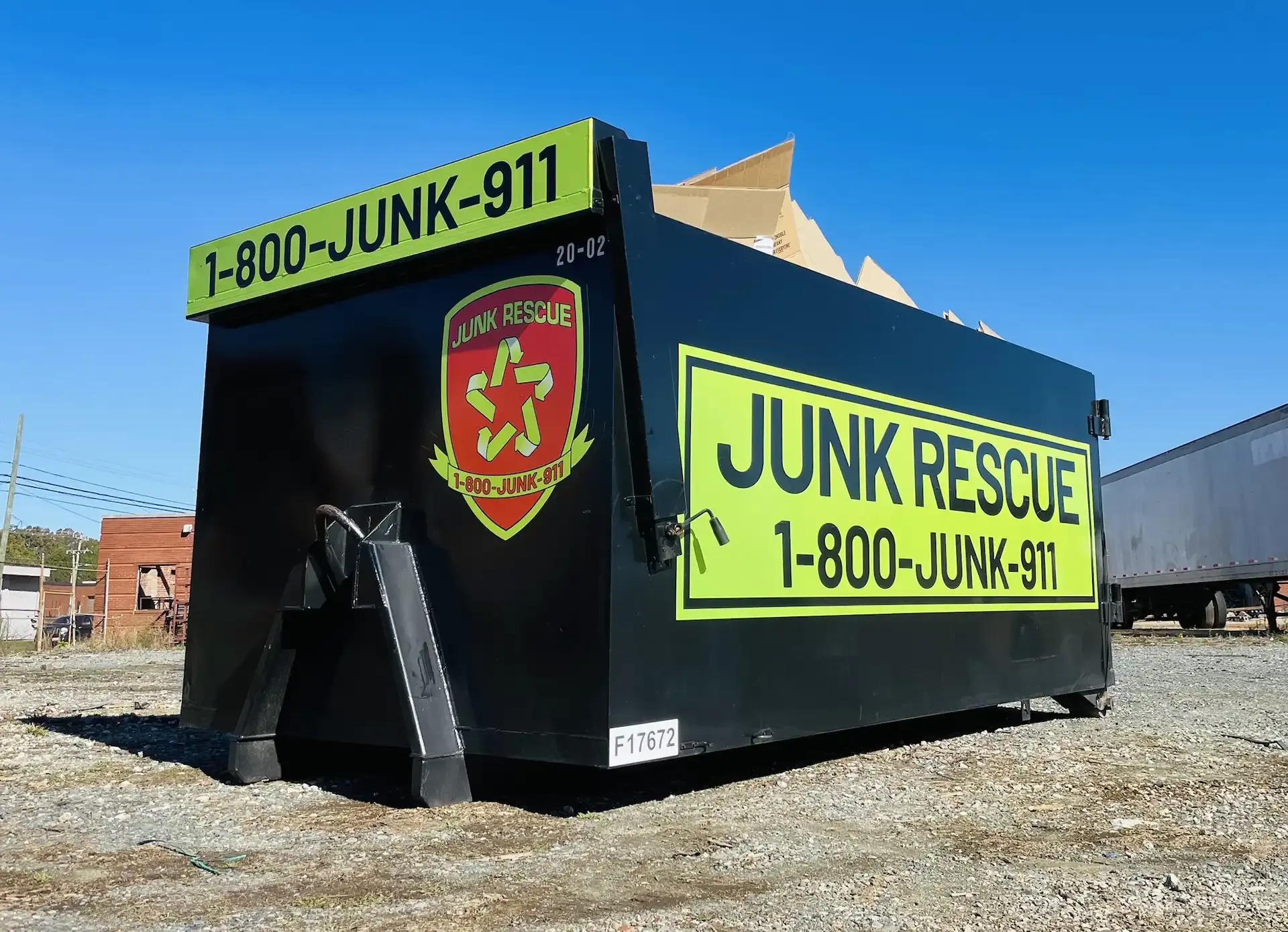 Black Junk Rescue dumpster with yellow text and logo, containing debris, outdoors.