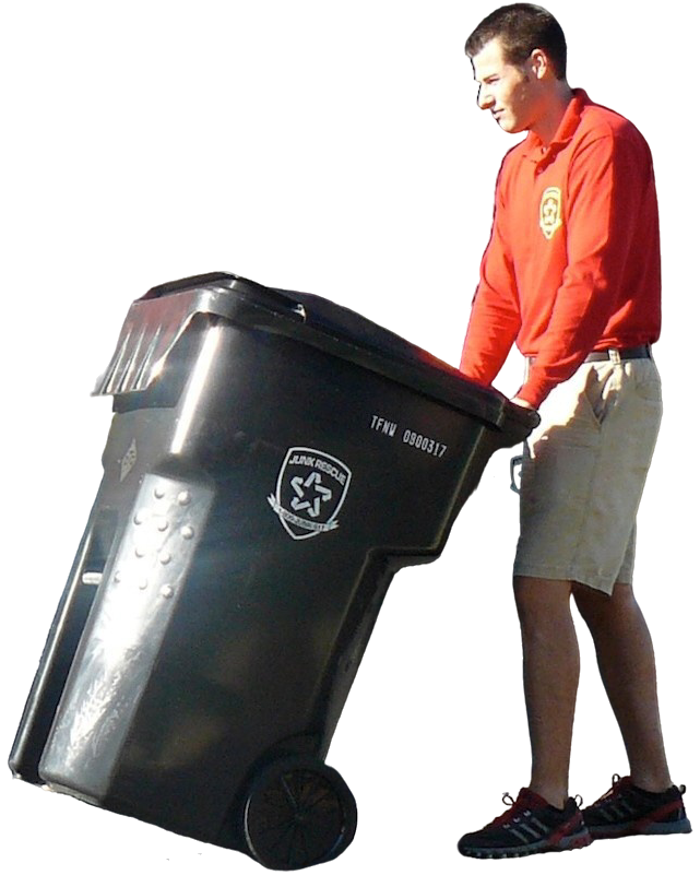 Man in red shirt and shorts rolling a black trash bin with wheels.