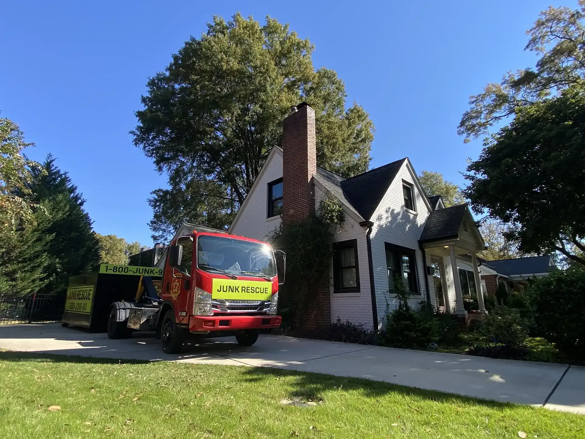 Red dump truck parked in front of a white house with a brick chimney on a sunny day.
