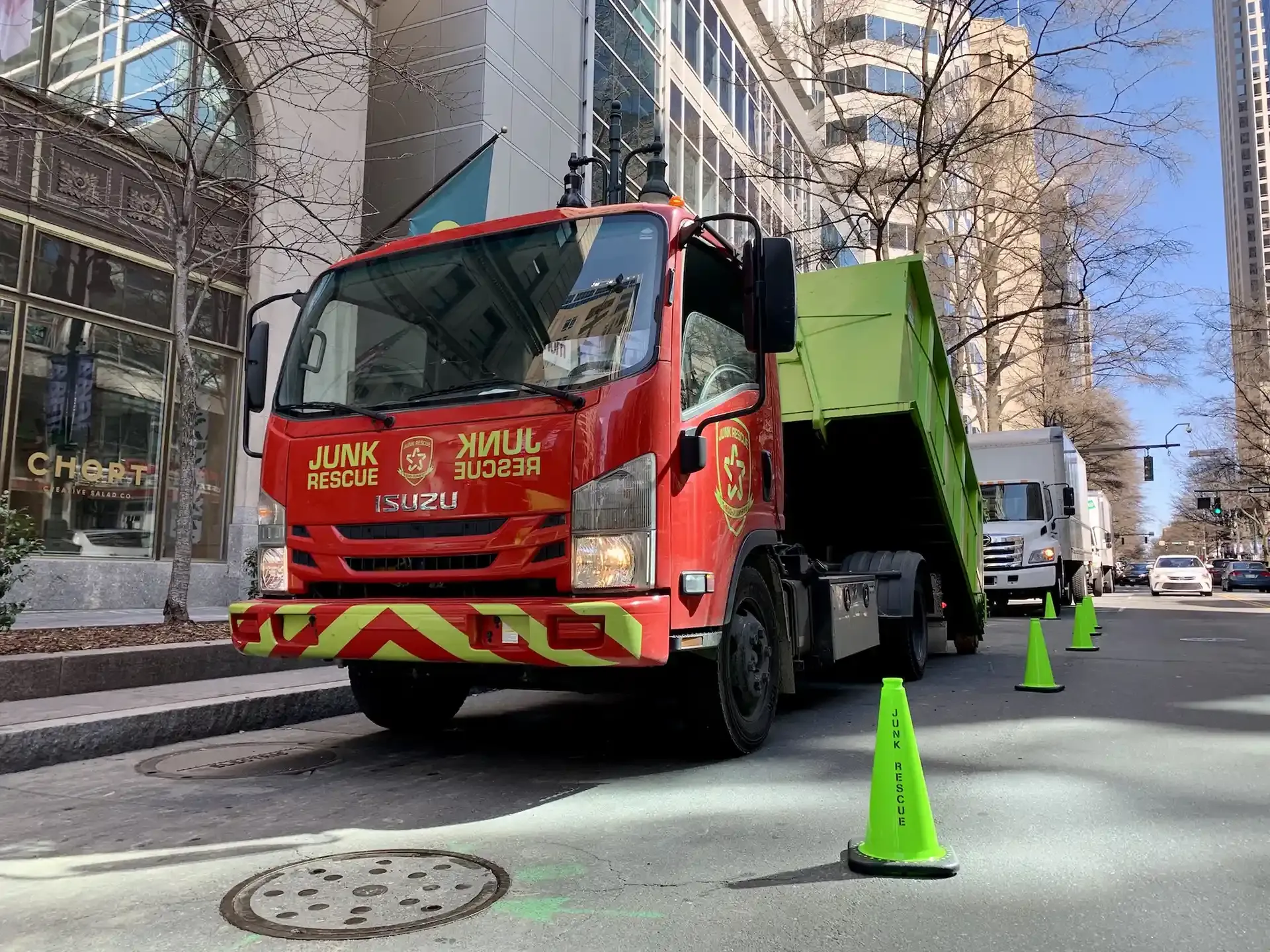 Red Junk Rescue truck with green dumpster on city street, traffic cones nearby.