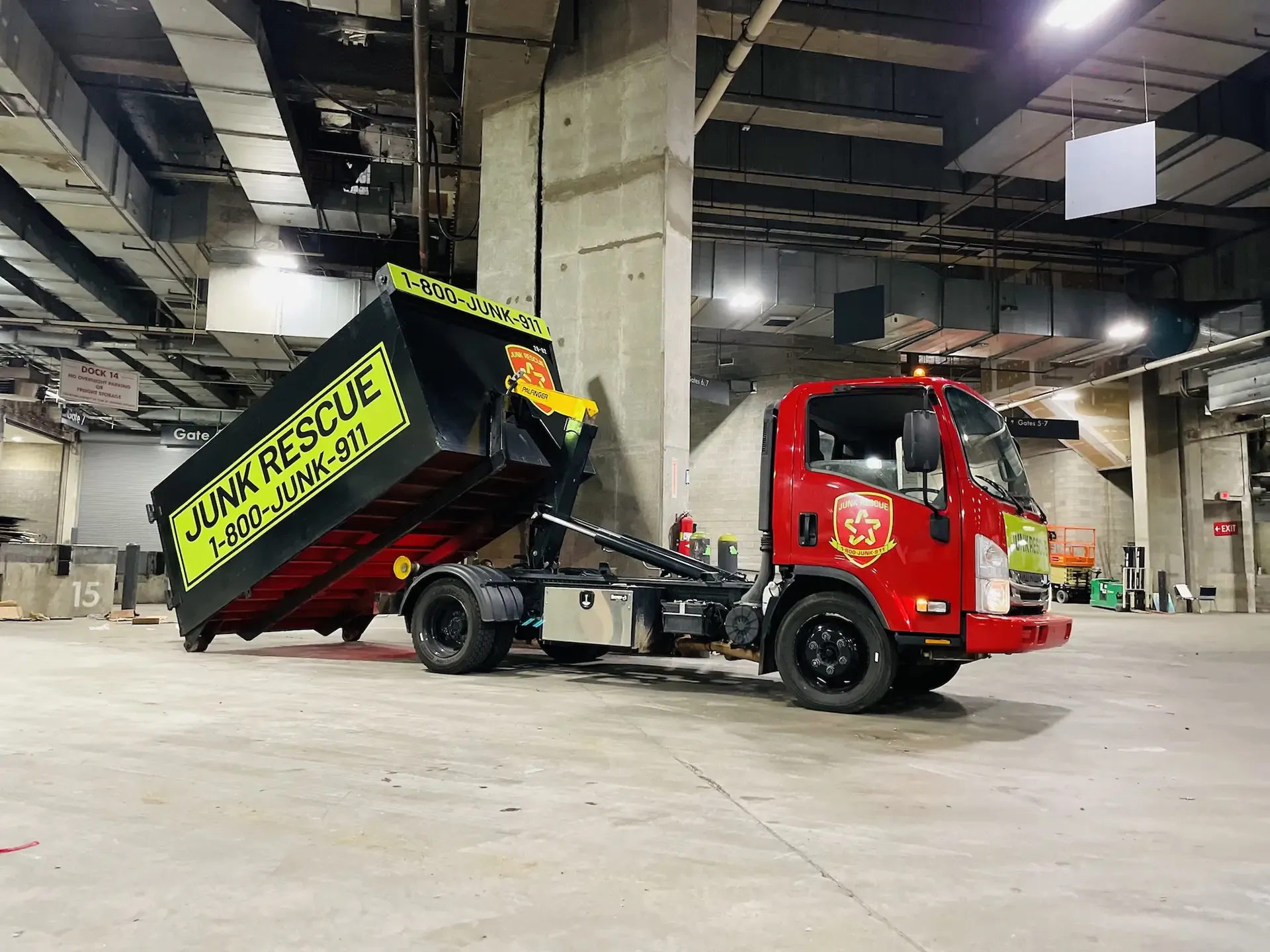 Red Junk Rescue truck with black dumpster in an industrial space.