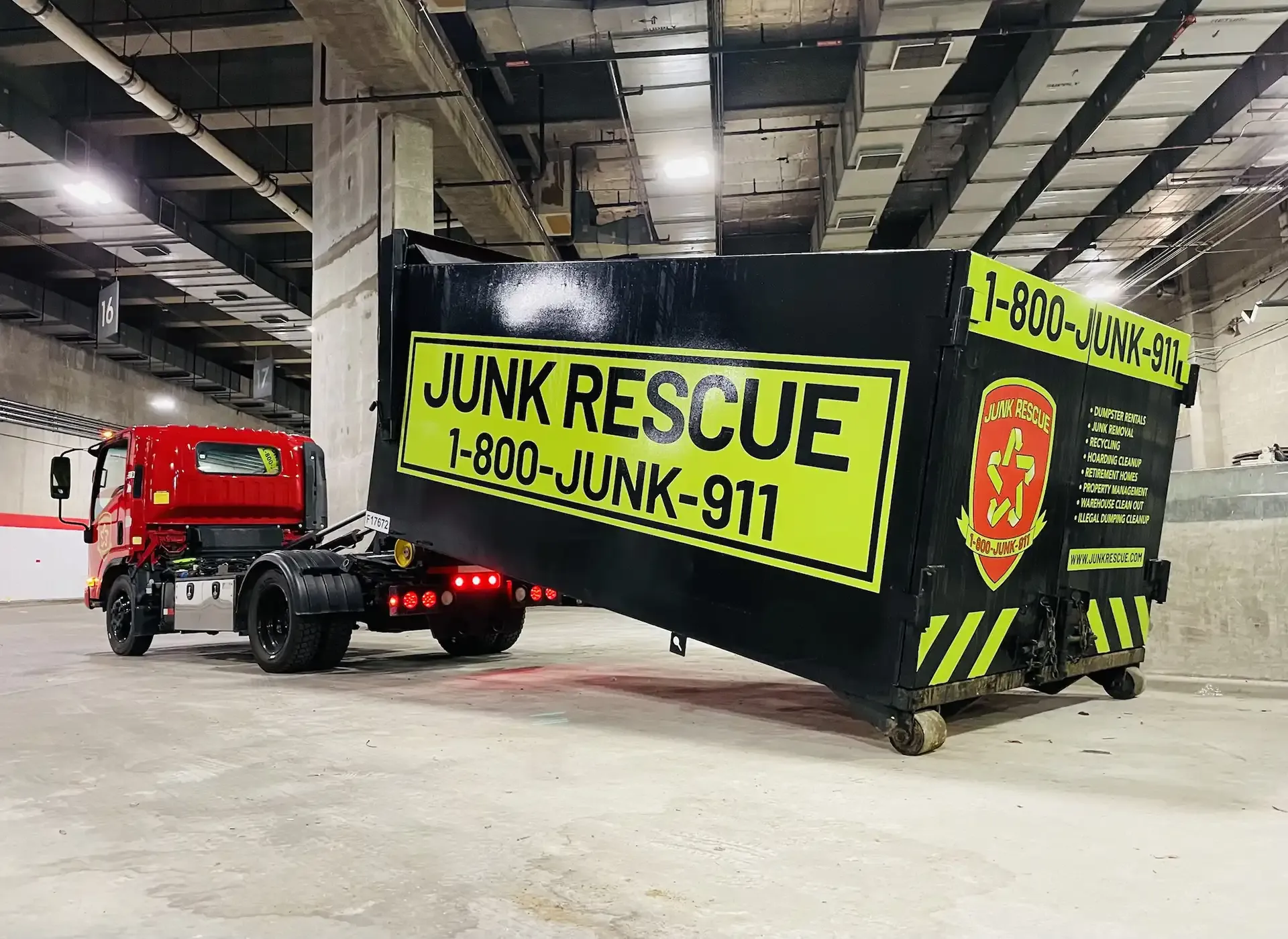 Black and yellow Junk Rescue dumpster on a truck inside a building. Phone number visible.