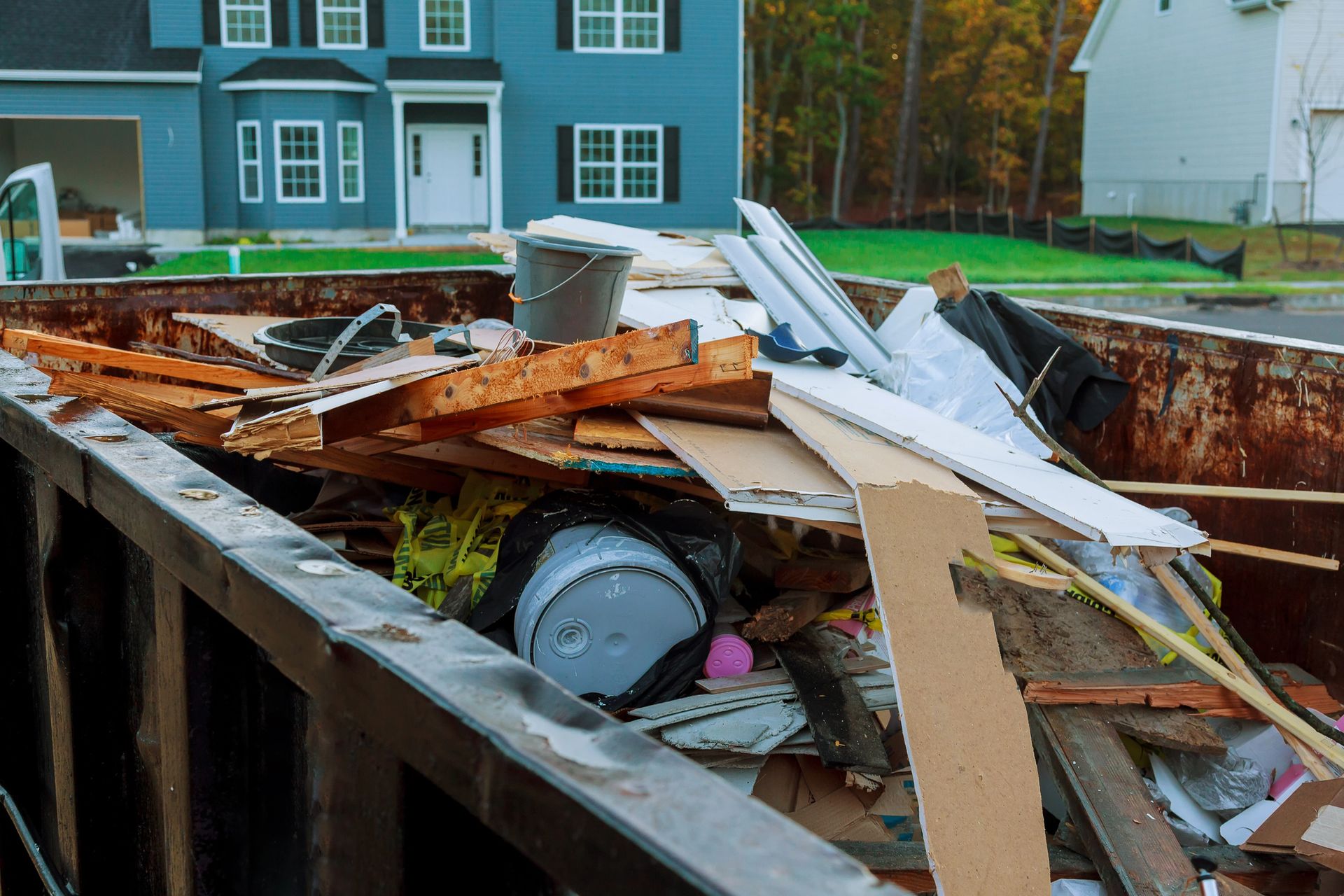 Overflowing dumpster full of wood, metal, and debris in front of houses