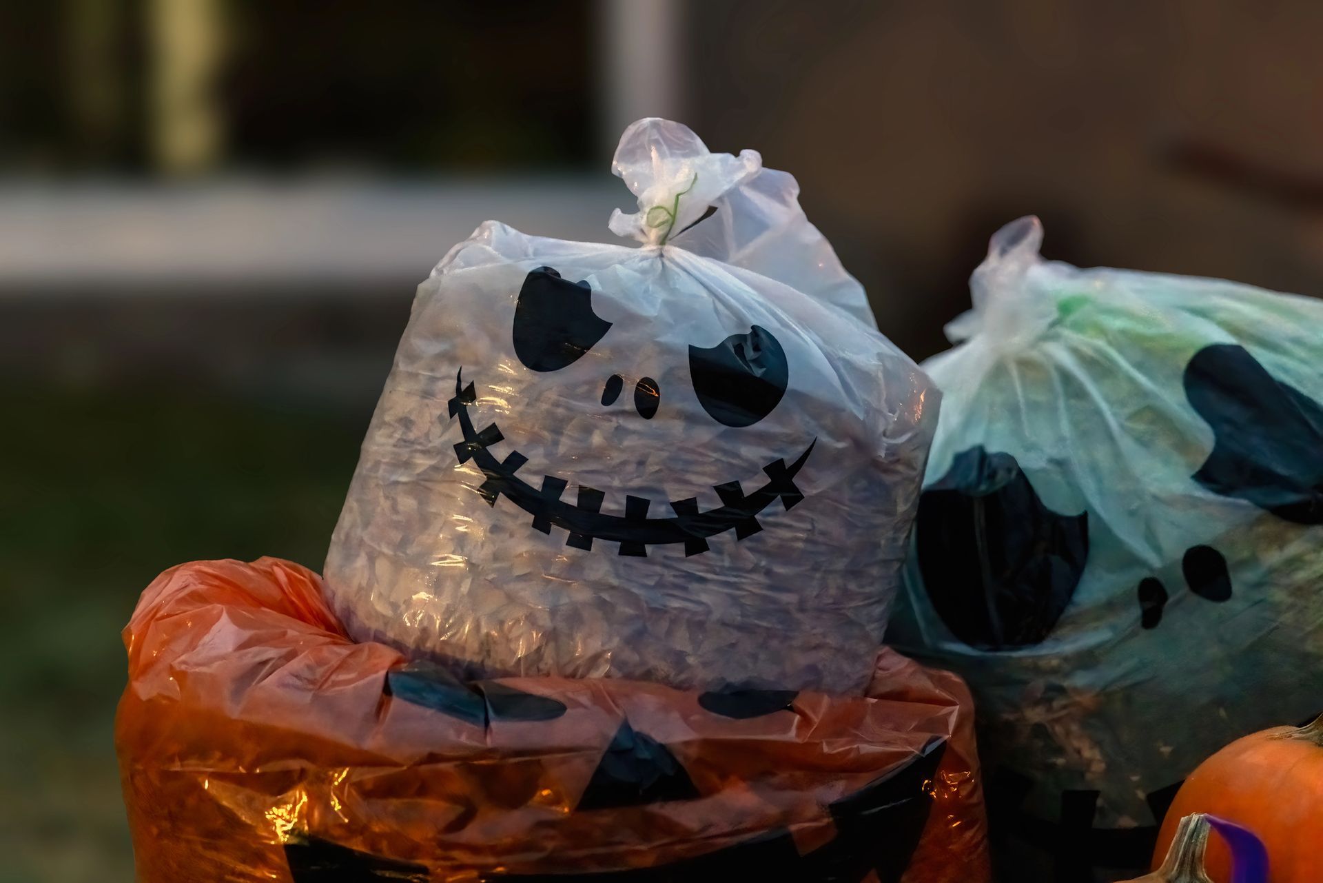 Pumpkin-style plastic trash bags with spooky faces, including orange and white bags, outdoors at dusk