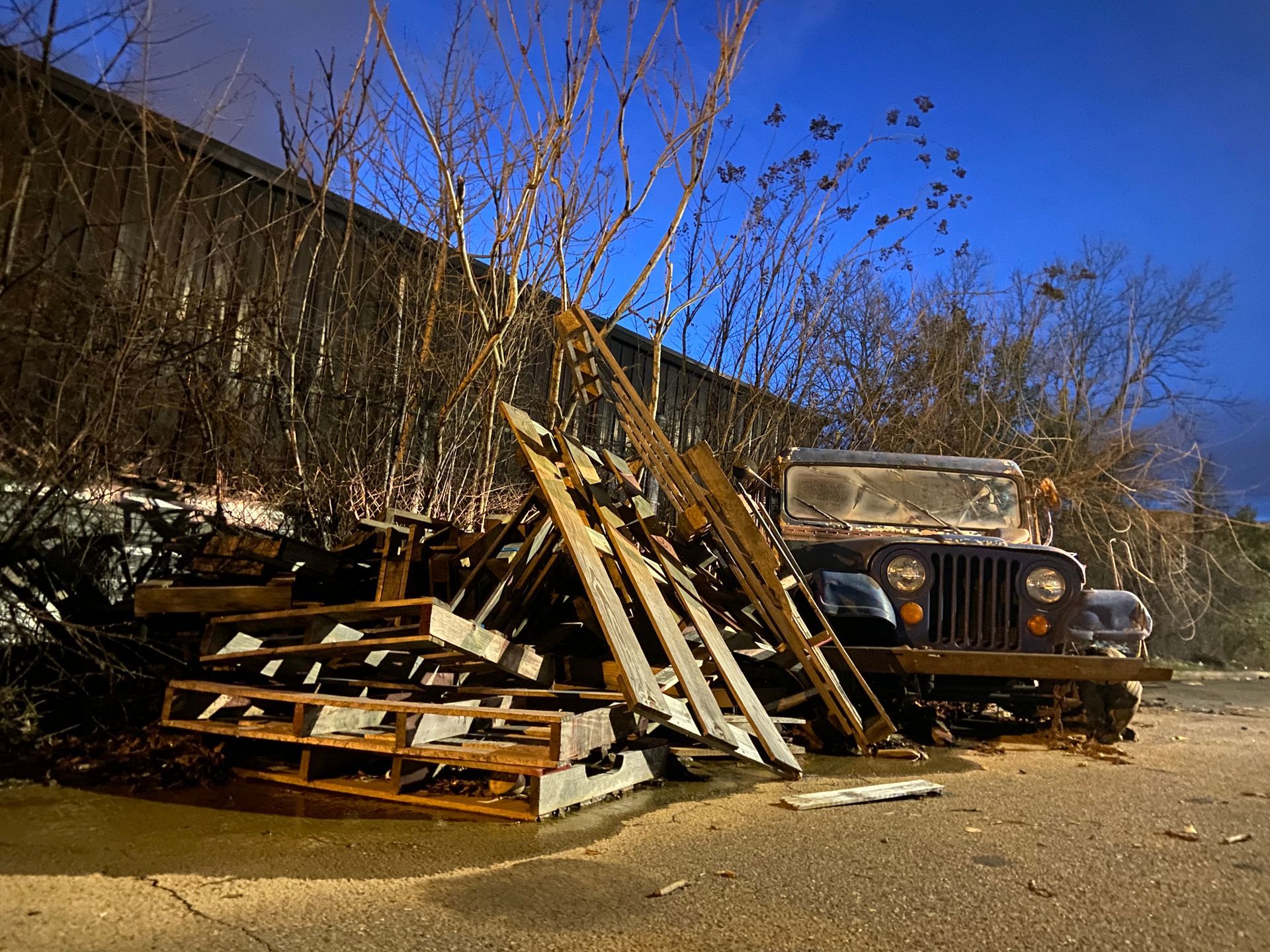 Blake Redden An old, rusty Jeep and wood pallets are next to a building under a blue twilight sky.