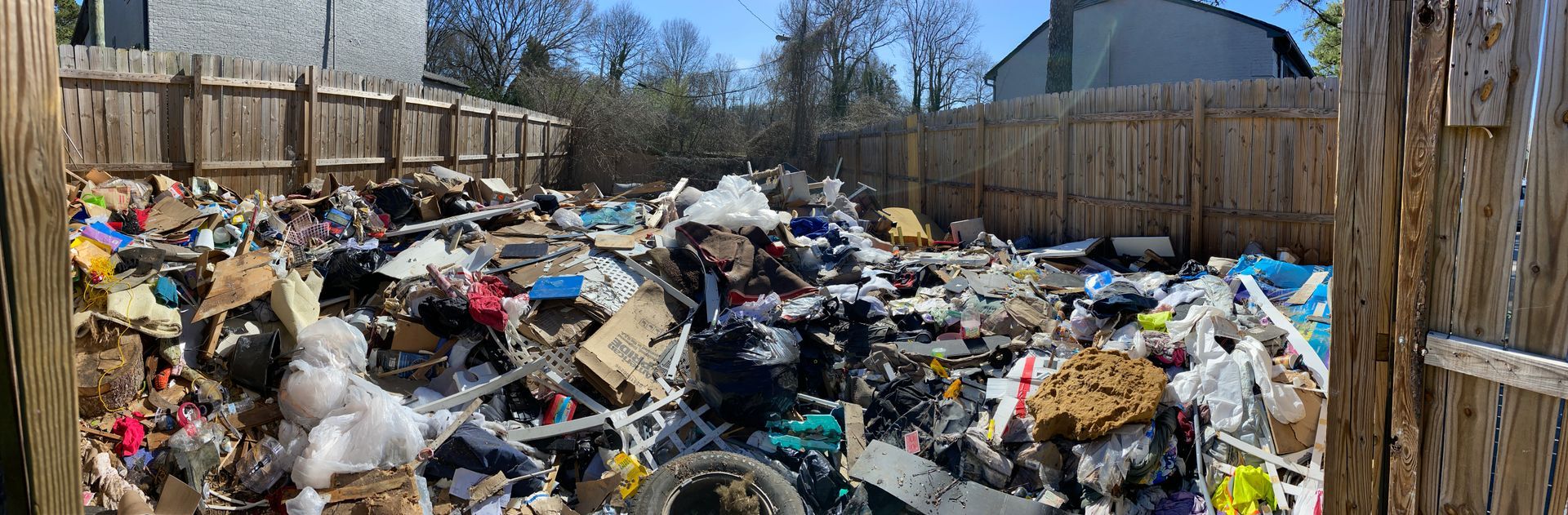 A large backyard filled with a massive pile of trash and debris, surrounded by a wooden fence.