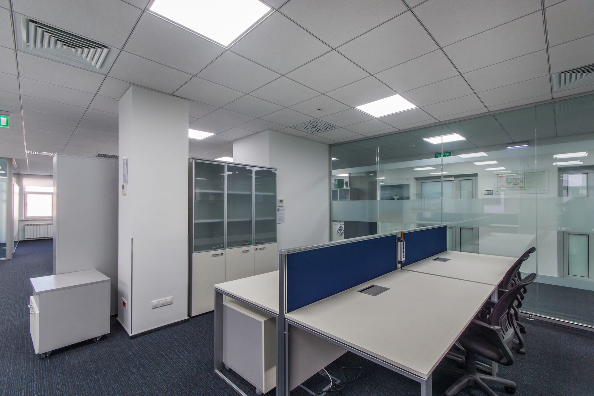 Empty office space with desks, storage cabinets, and glass partitions.