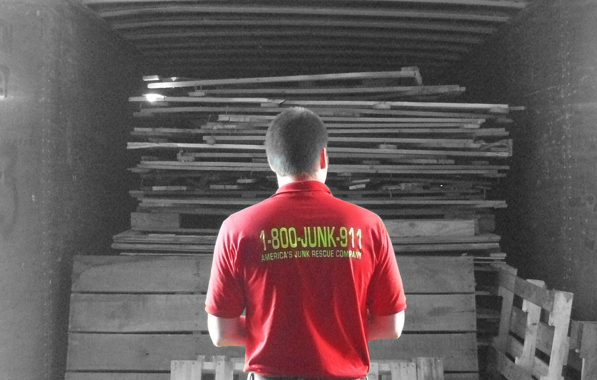 Man in red shirt with 1-800-JUNK-911 logo looking at a pile of wood inside a truck.