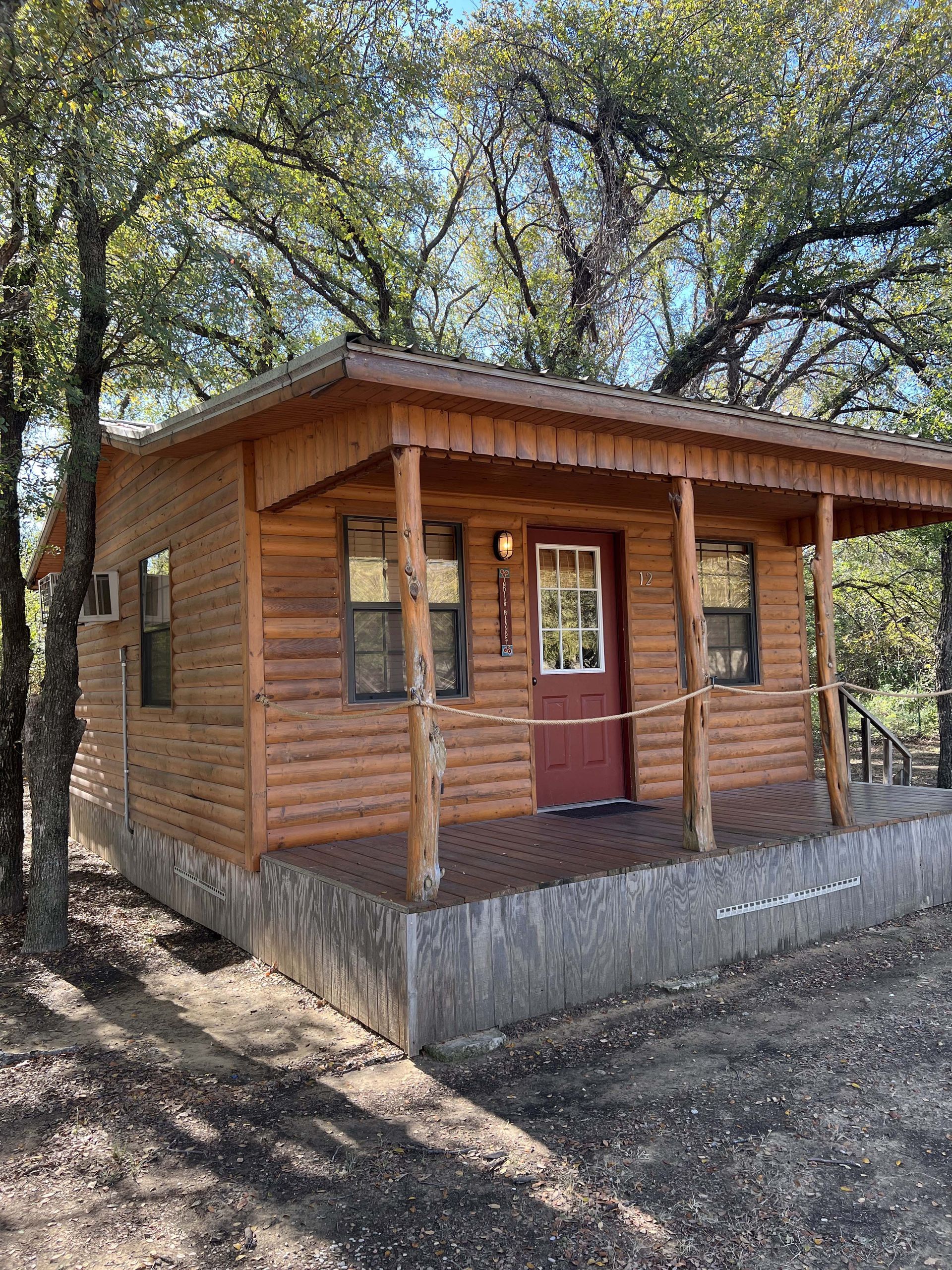A small log cabin with a red door and porch surrounded by trees.