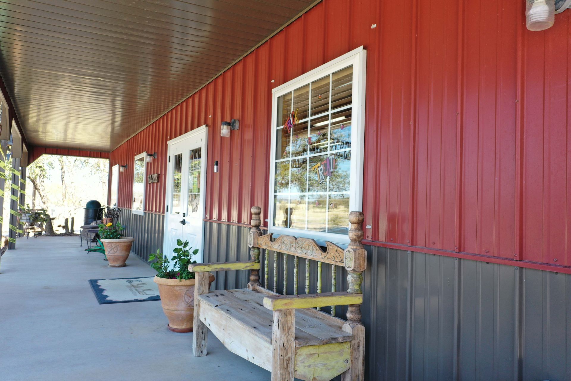 A wooden bench is sitting on a porch next to a red building.