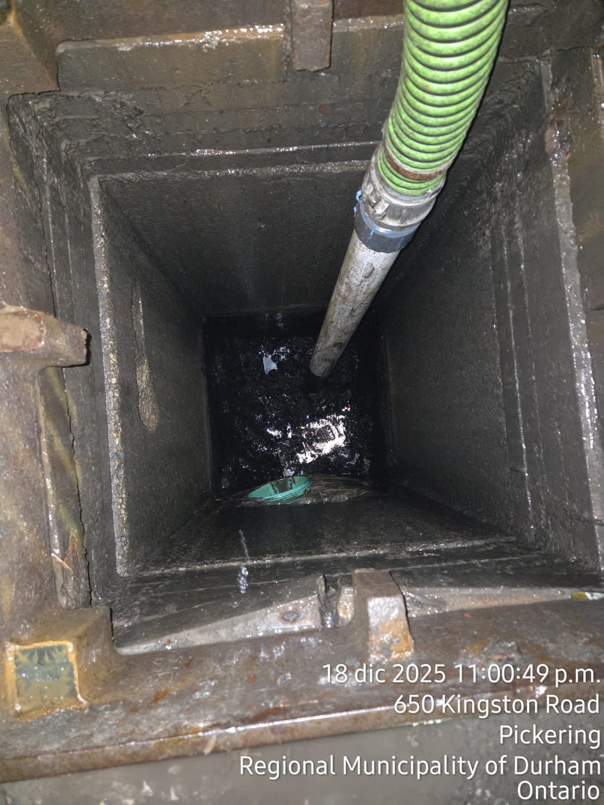 Looking down into a dark, water-filled industrial drain. A green hose extends down into it.